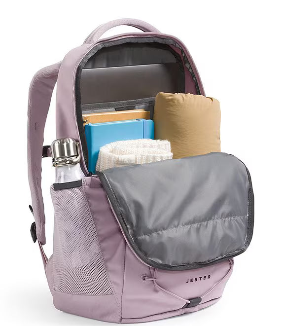 A lavender Jester backpack shown open, revealing its interior storage capacity with a gray padded compartment, a water bottle in the side mesh pocket, and packed items inside, on a white background.