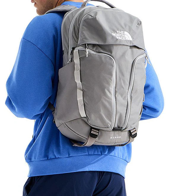 A person wearing a blue sweatshirt and navy pants shown from the back, carrying a gray The North Face X-2000 backpack against a white background.