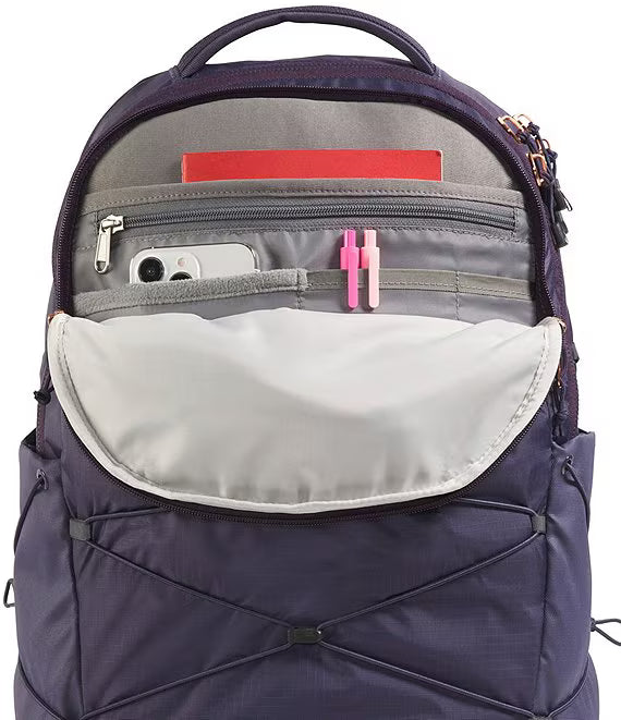 A navy blue backpack with its front flap open, showing a light gray interior pocket, a phone in the side pocket, and pink and red accessories. The backpack is photographed on a clean white background.