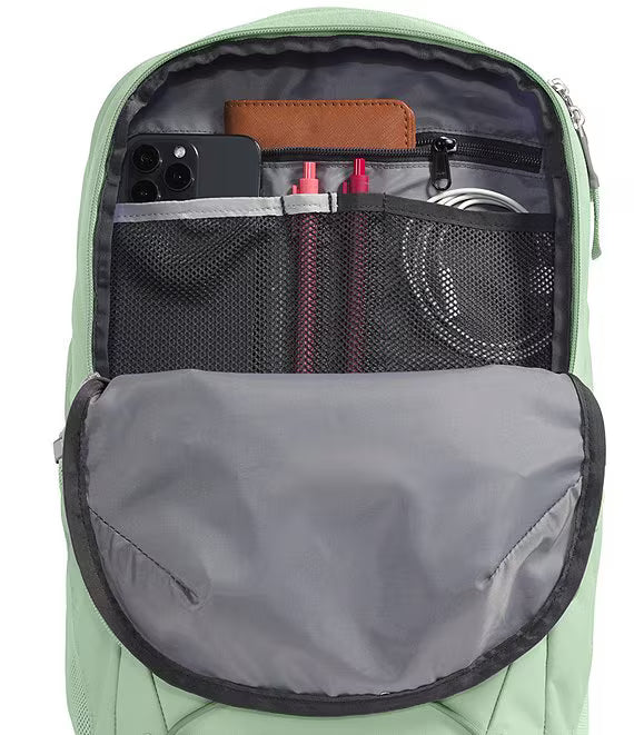 Open sage green backpack showing the interior organization with mesh pockets, zip compartments, a phone, pens, and accessories, on a white background.