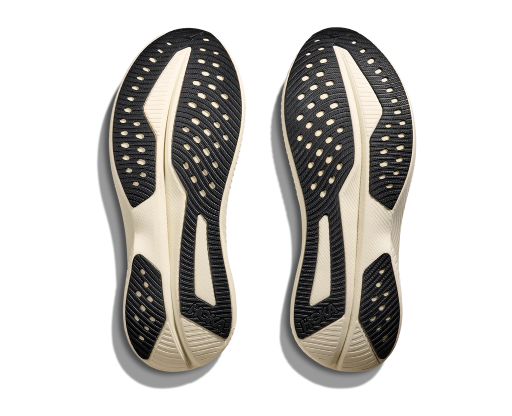 A pair of athletic shoe soles shown from the bottom, featuring a black and off-white design with textured grip patterns and circular cutouts, photographed on a white background with soft drop shadows.