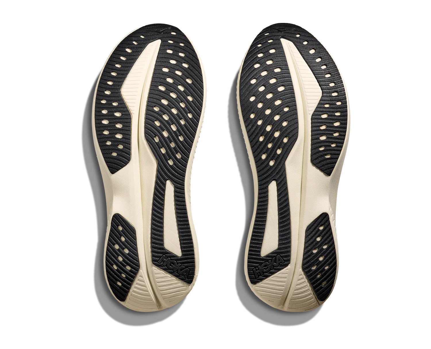 A pair of athletic shoe soles shown from the bottom, featuring a black and off-white design with textured grip patterns and circular cutouts, photographed on a white background with soft drop shadows.