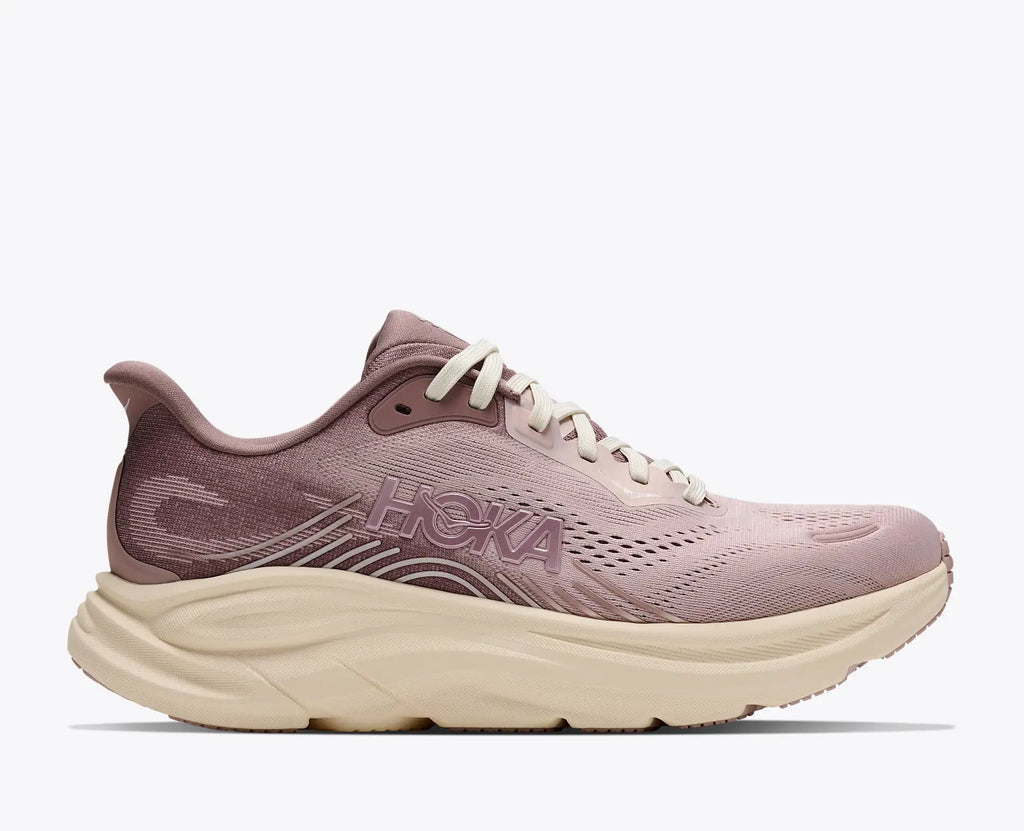 A Hoka running shoe in a dusty mauve pink colorway with a chunky cream-colored midsole and white laces, shown from a side profile on a light gray background.