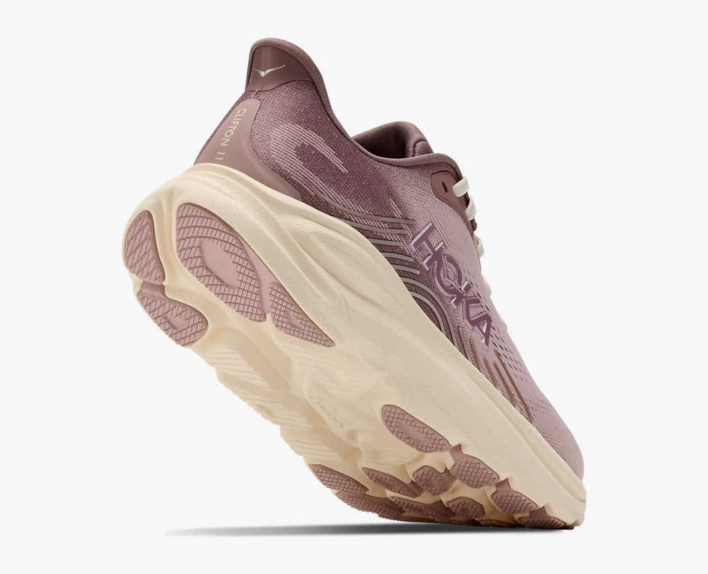 A Hoka running shoe in a dusty mauve color with a thick cream-colored midsole, shown from a three-quarters angle against a light gray background.
