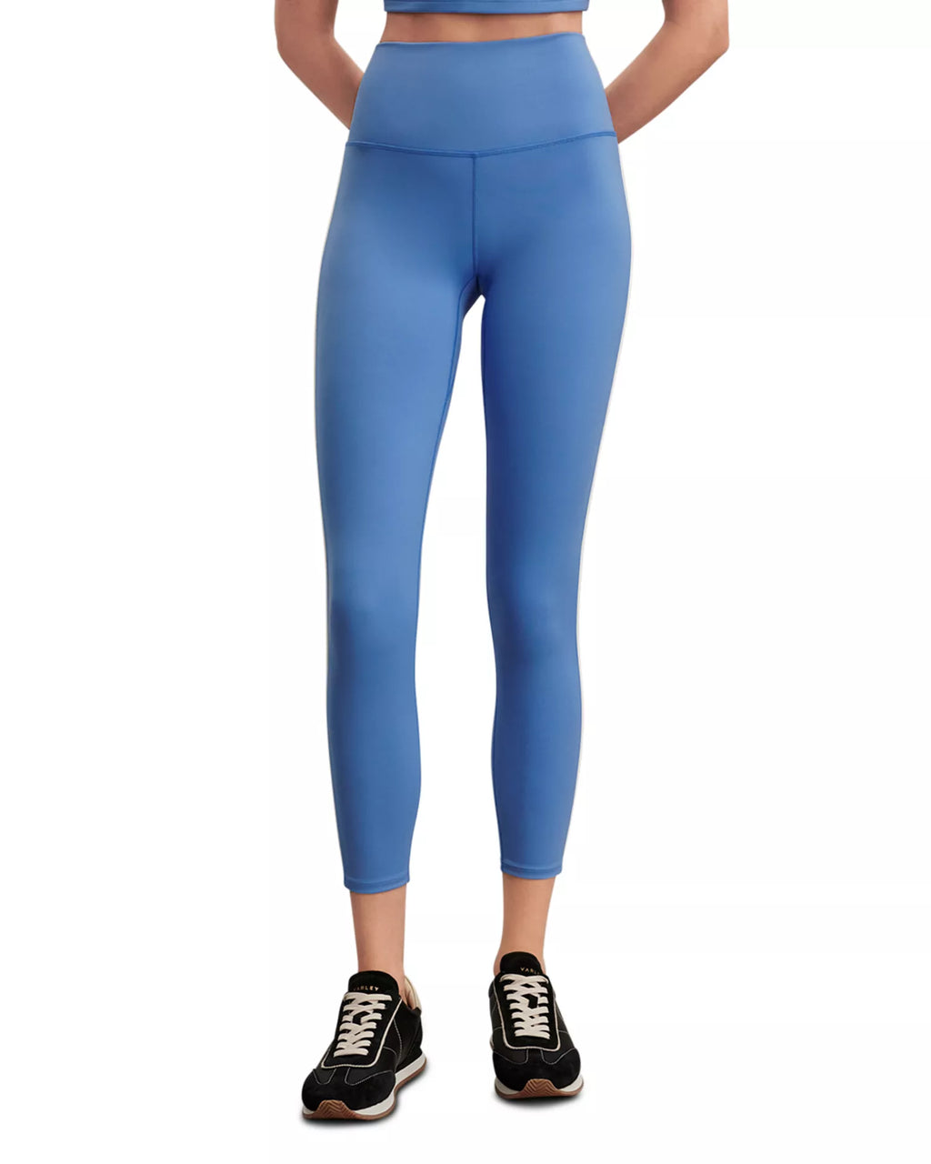 A person wearing high-waisted blue leggings and black athletic sneakers, shown from the waist down against a plain white background.