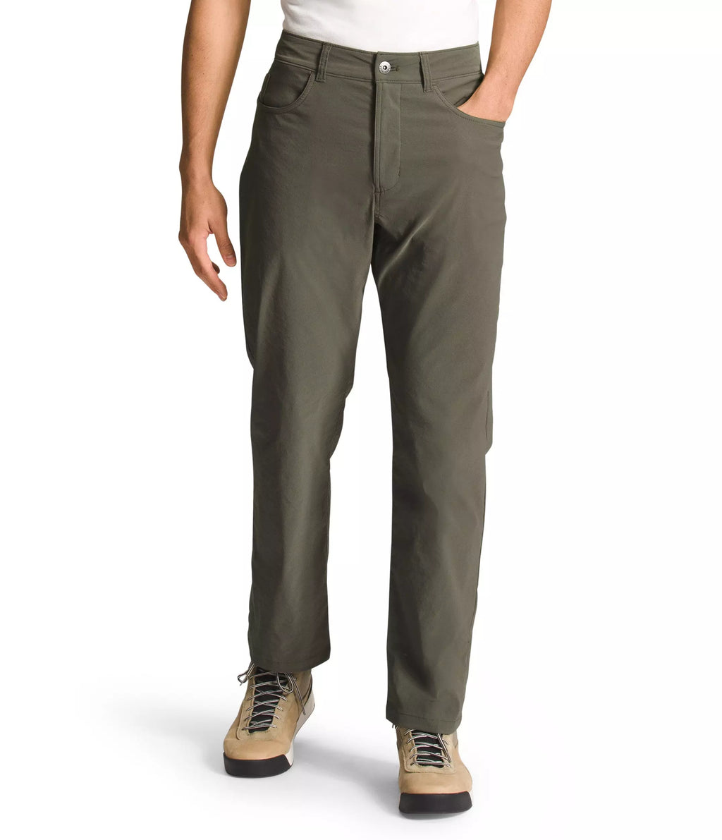 A person wearing olive green straight-leg pants, a white t-shirt, and tan lace-up boots, shown from the waist down against a plain white background.