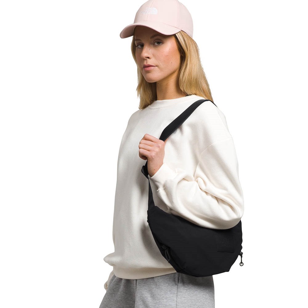 Woman wearing a white sweatshirt, gray pants, and a pink cap with a black crossbody bag on a white background