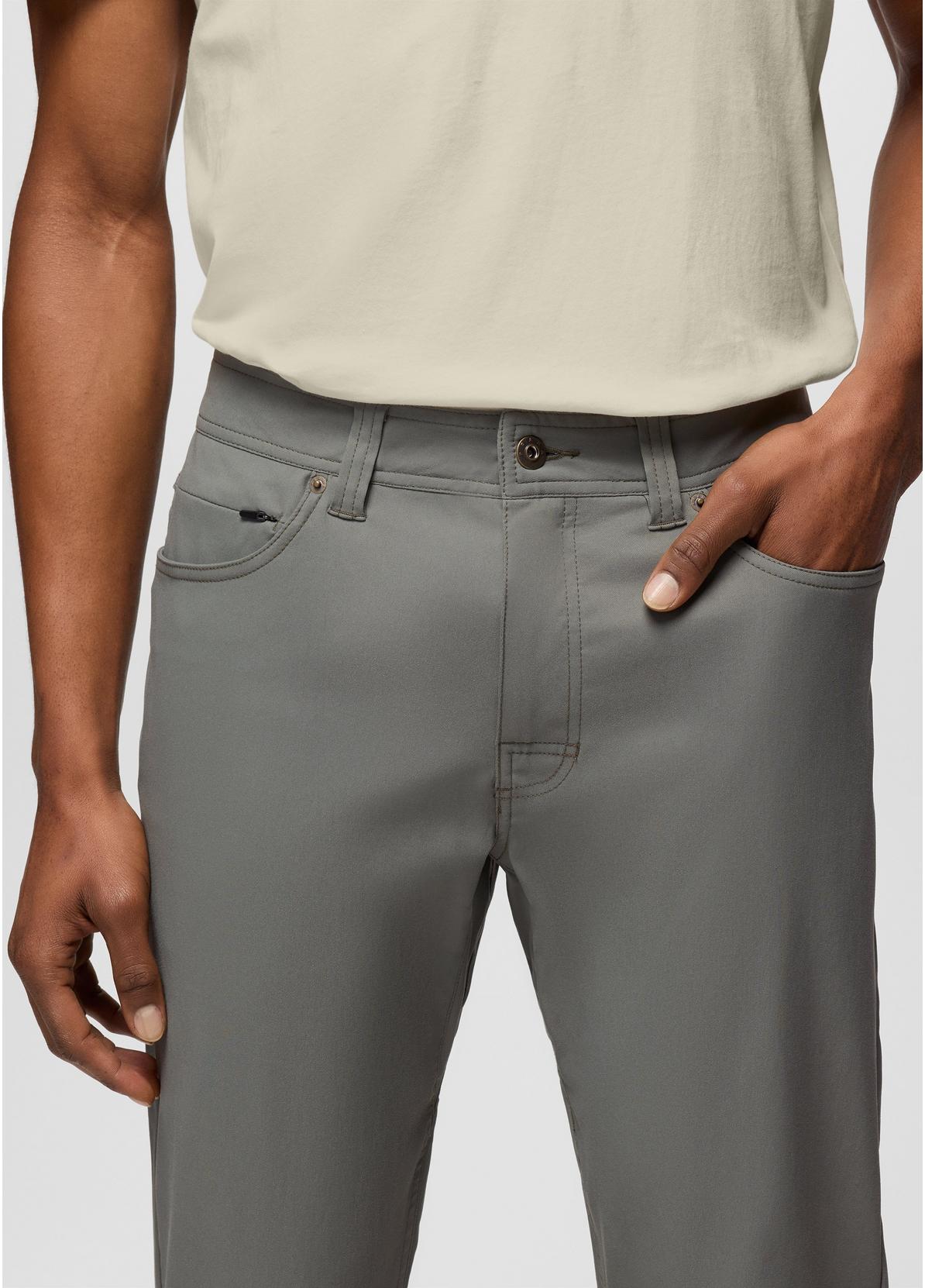 A close-up of a person wearing gray slim-fit trousers with a light beige t-shirt, showing the front pockets and waistband details.