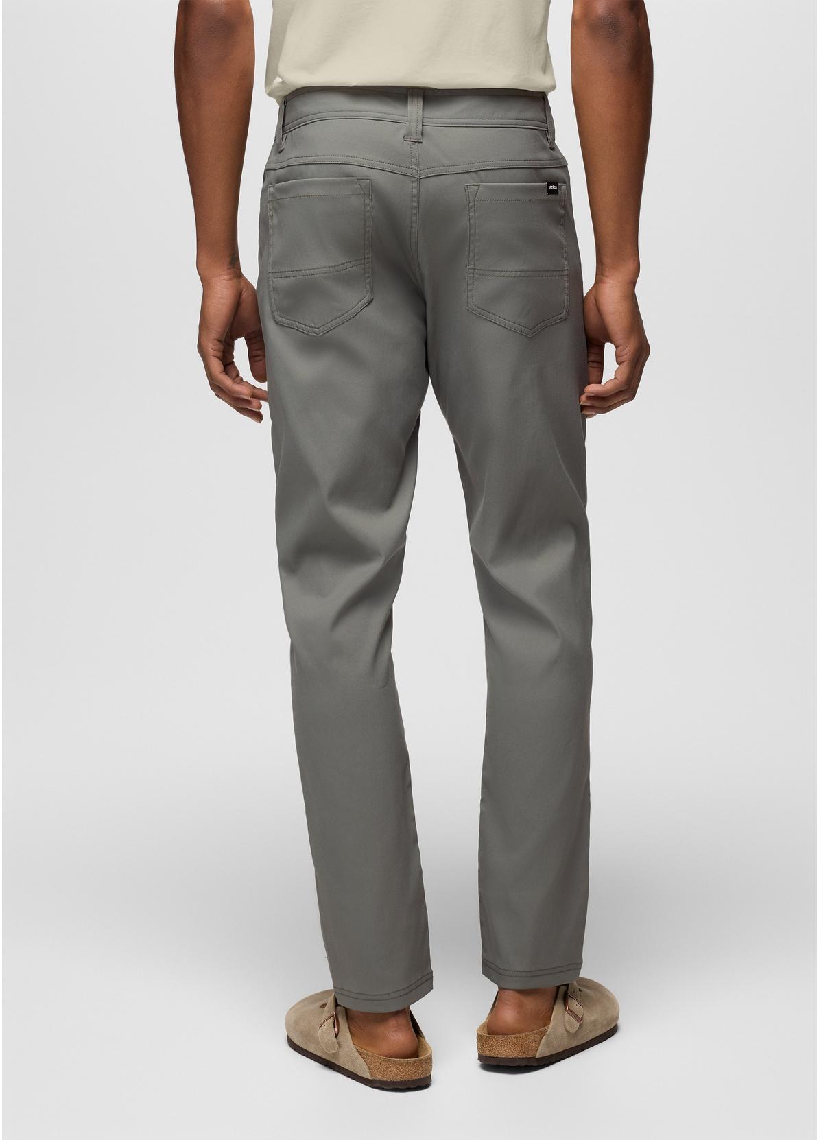 A person shown from the back wearing gray straight-leg pants, a light beige top, and tan slide sandals against a light gray studio background.