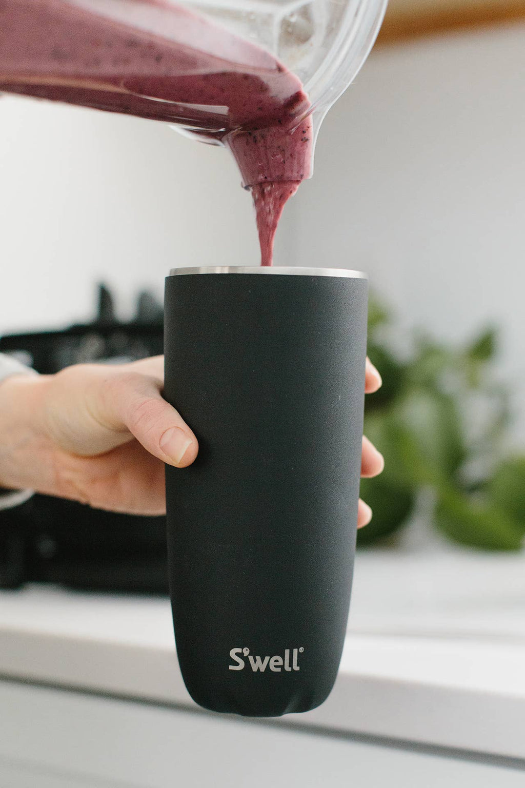 Red liquid being poured into a black 'S'well' tumbler on a white surface.