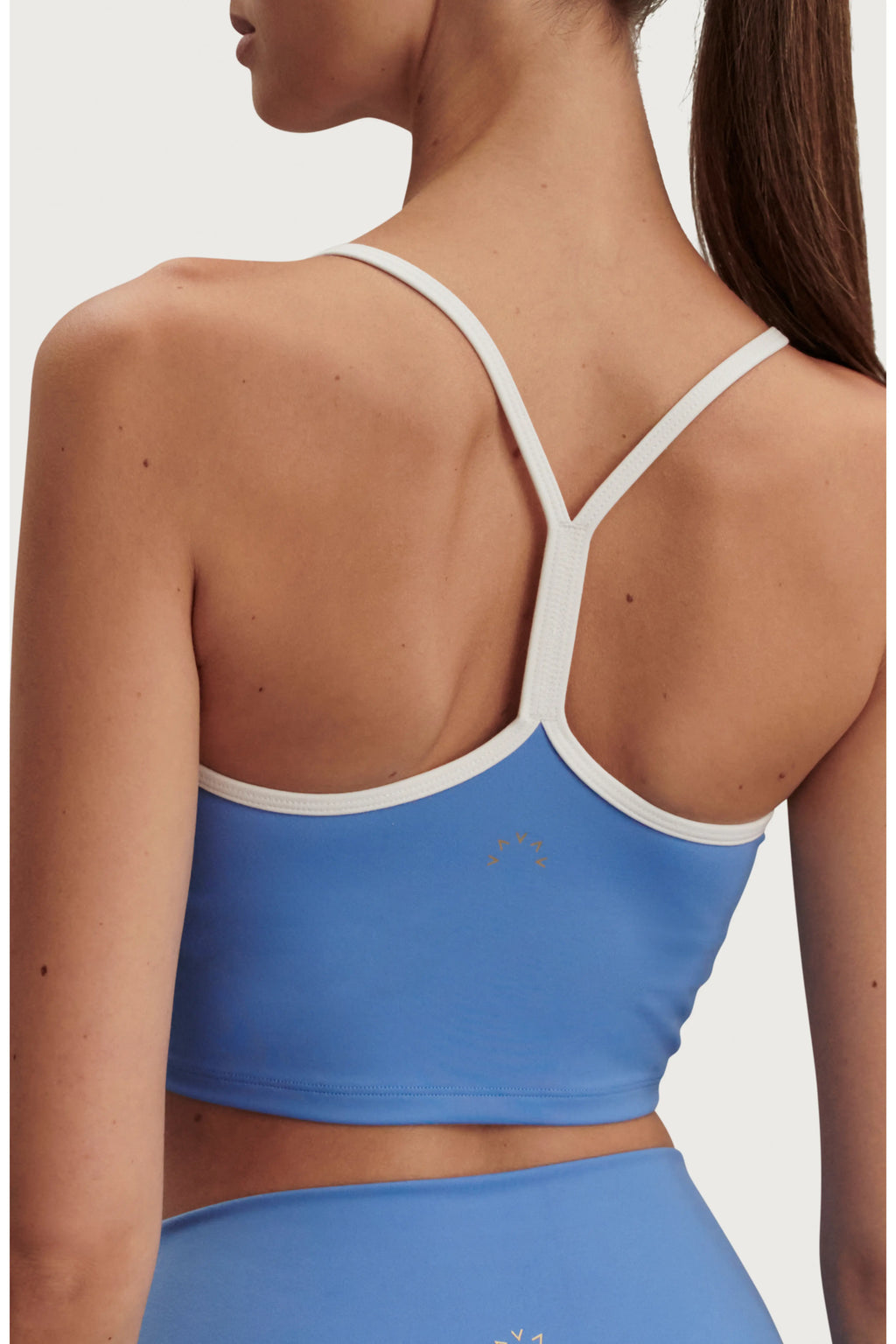 A woman shown from the back wearing a light blue sports bra with contrasting white trim and thin crisscross shoulder straps, paired with matching blue bottoms against a plain light background.