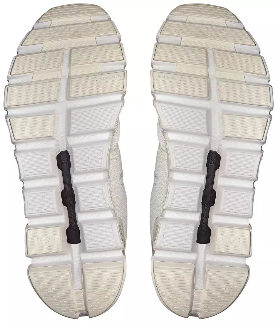 The outsoles of a pair of white athletic shoes, showing the textured grip pattern and black heel pull tabs, isolated on a white background.