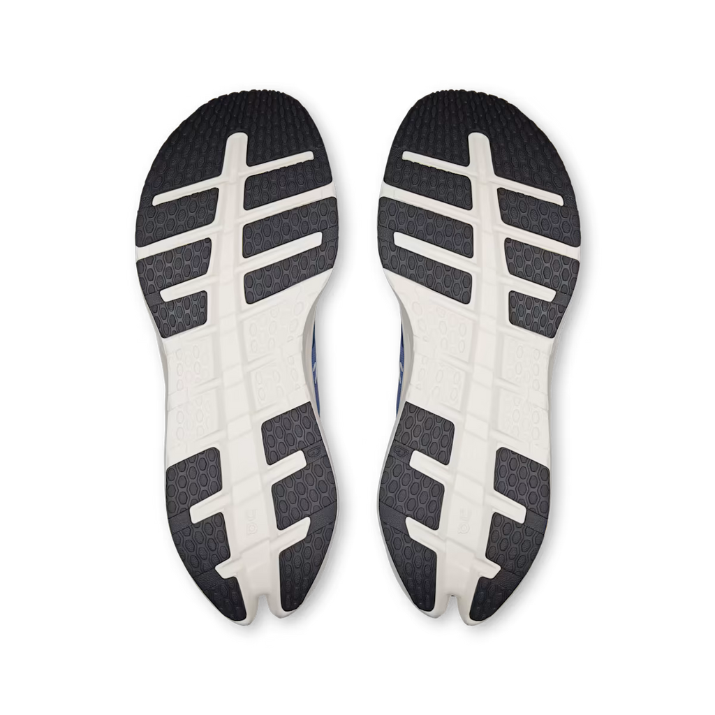 A pair of athletic shoes shown from the bottom, displaying their black and white textured outsoles against a plain white background.