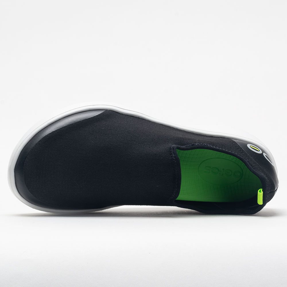 Black slip-on shoe with green sole on a white background