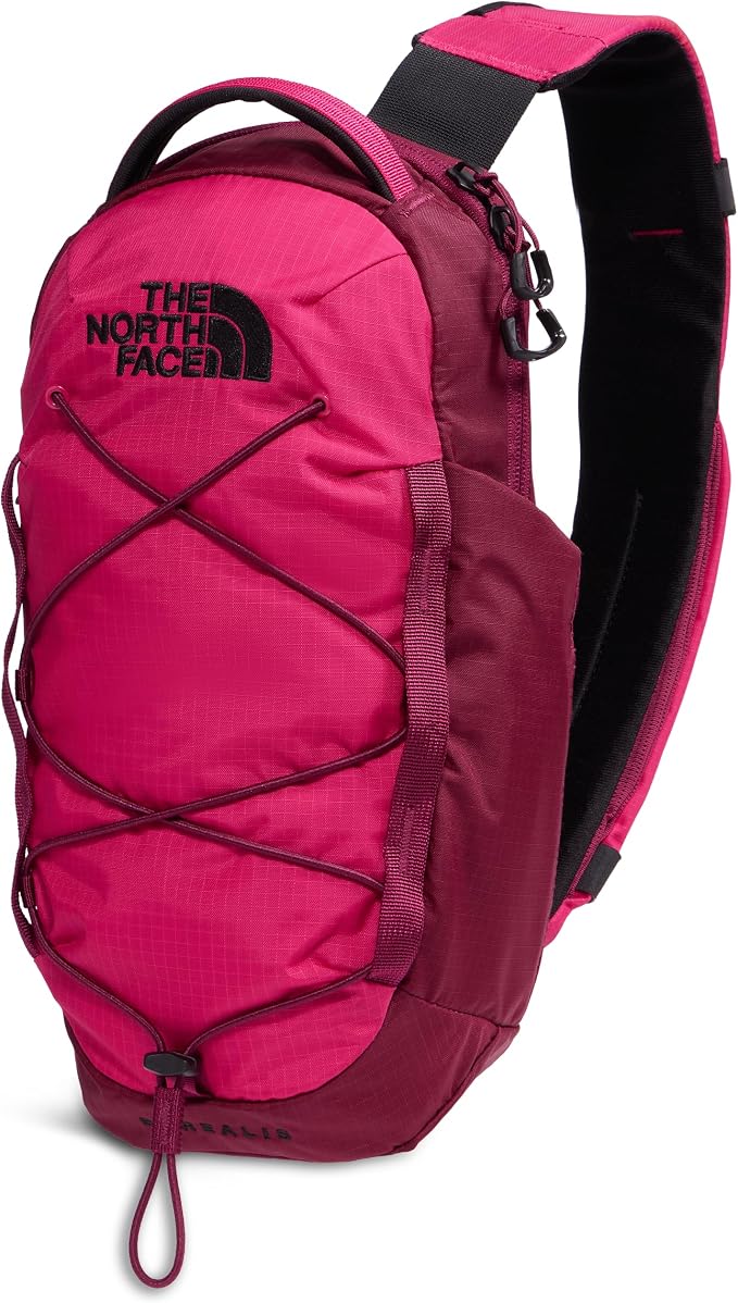 A The North Face sling backpack in a vibrant magenta pink color, featuring a black logo on the front, crisscross lacing details, and a black padded shoulder strap, shown against a plain white background.