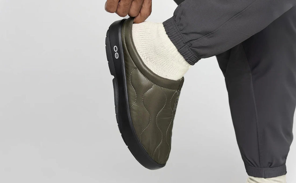 Person wearing a green slipper with a textured sole on a light gray background