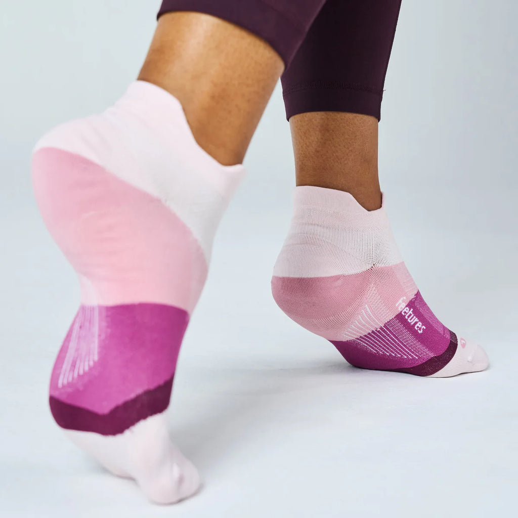 A close-up of a person's feet wearing low-cut athletic socks in pink, purple, and white, with the brand name 'Skechers' visible on the side of one sock.