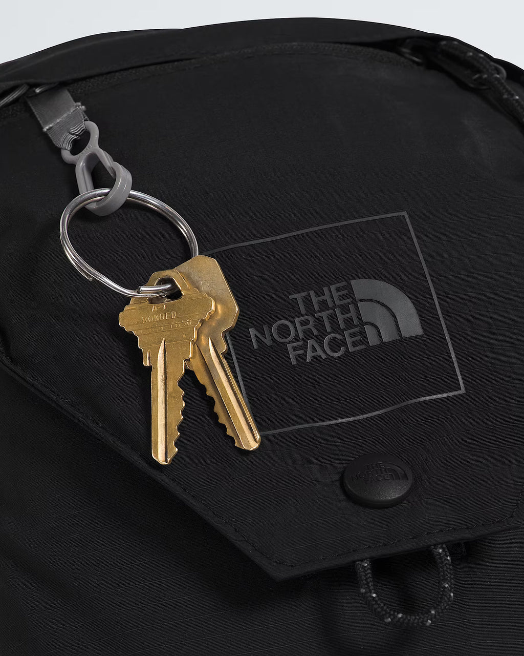 Close-up of a black The North Face bag with a key ring holding two brass keys, featuring the embossed brand logo on the flap.
