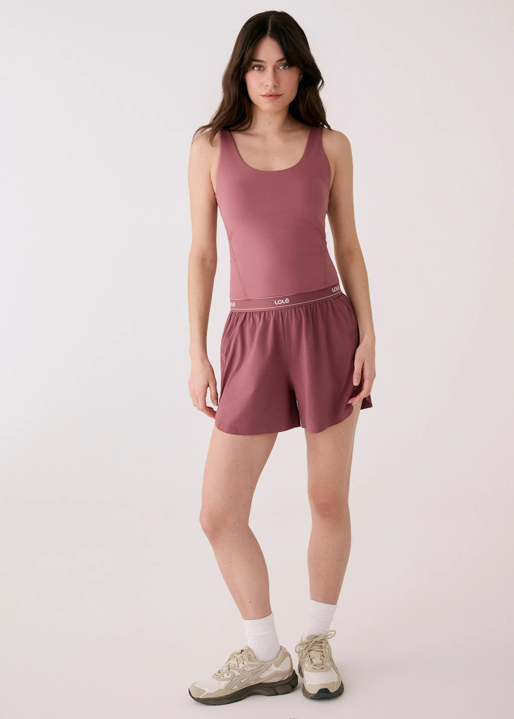 Woman wearing a mauve tank top and shorts on a white background
