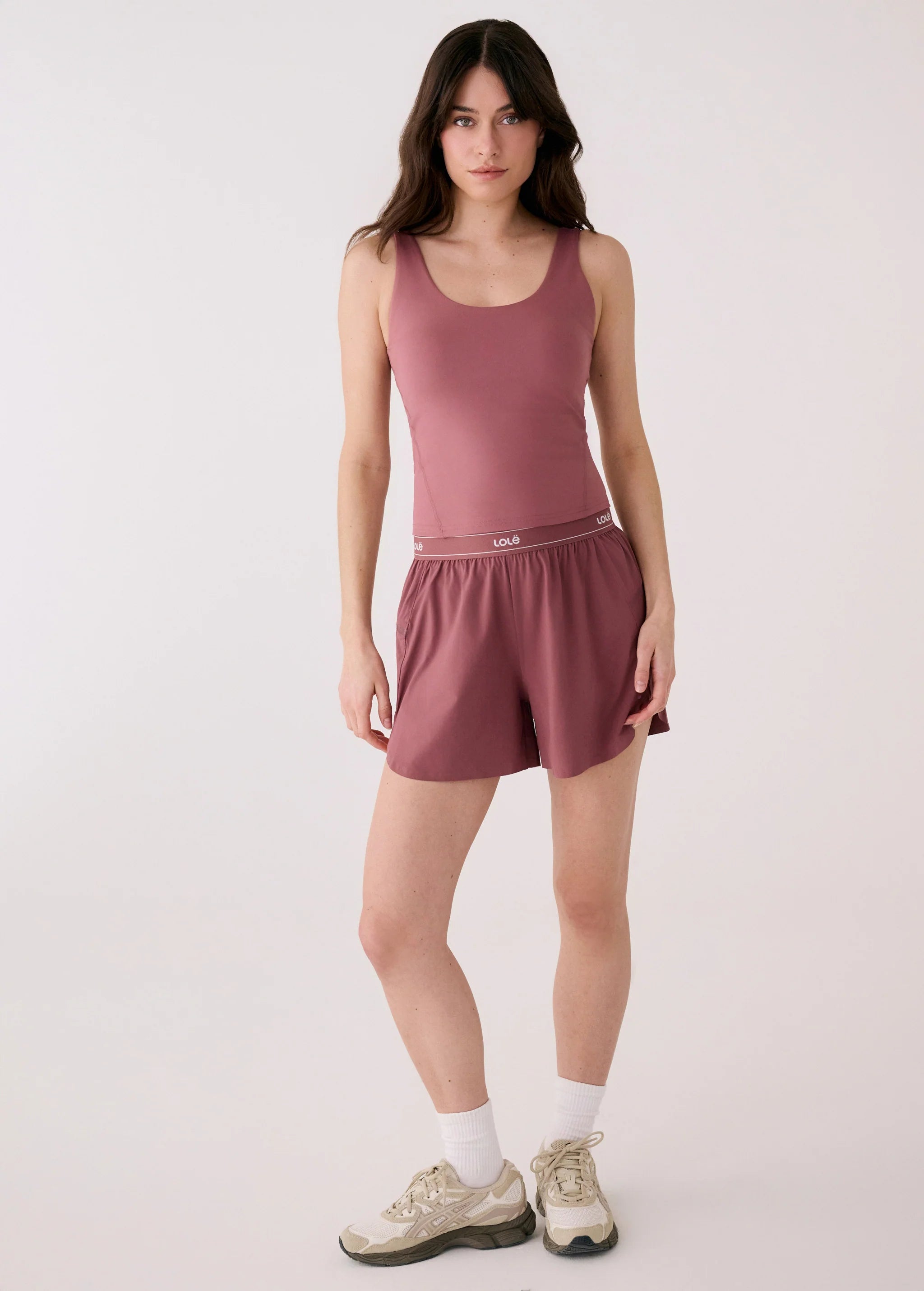 Woman wearing a mauve tank top and shorts on a white background