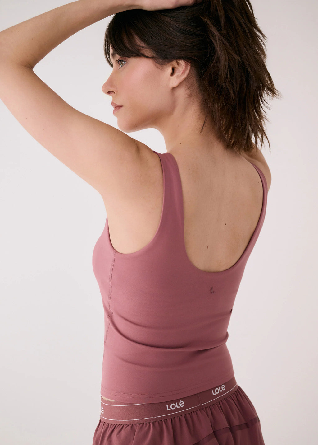 Woman wearing a mauve tank top with a visible brand logo on a plain background