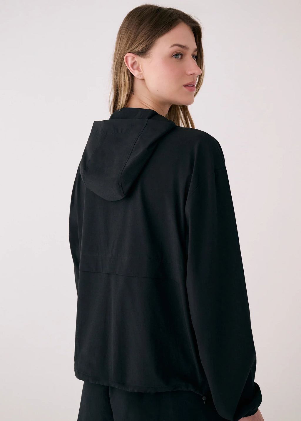 Woman wearing a black hooded jacket on a plain background