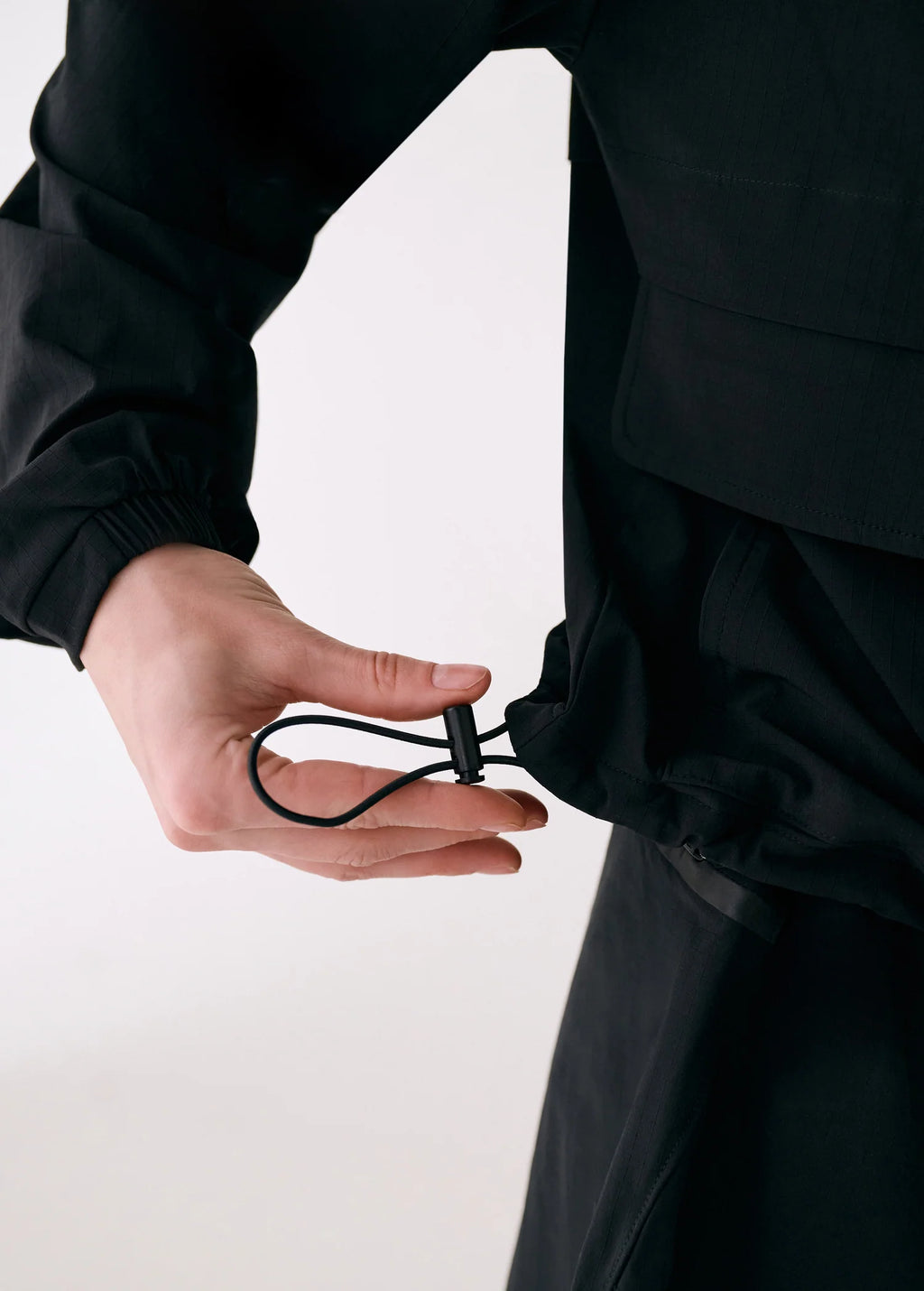 Person adjusting a black drawstring on a garment against a white background
