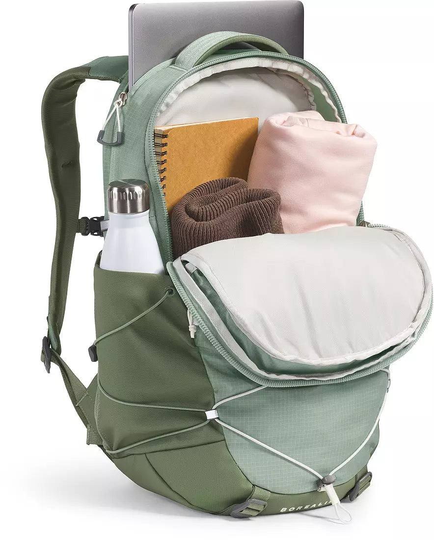 An olive green backpack shown open with a laptop, notebook, bottle, and folded clothing inside, photographed on a clean white background.