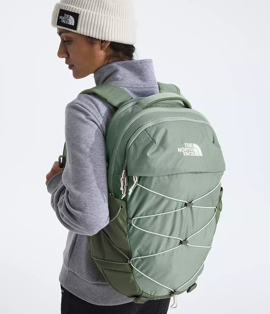 Person wearing a green backpack with The North Face logo on a light gray background