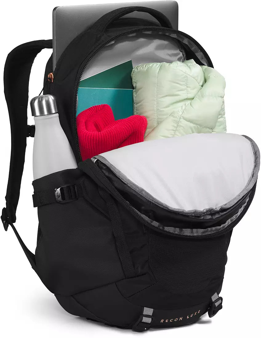 A black RECON LEAP backpack shown open, filled with a light green puffer jacket, a red knit item, a white bottle in the side pocket, and a gray laptop. The RECON LEAP logo is visible on the lower front.