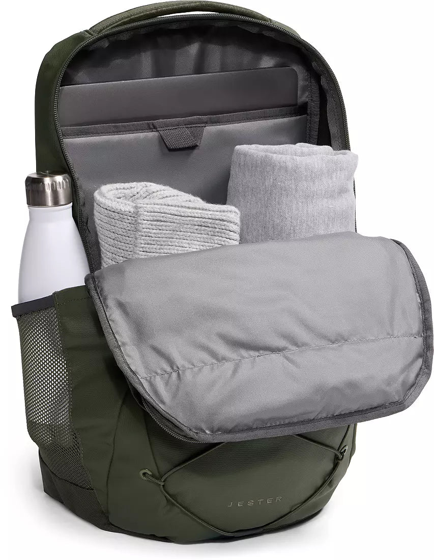 An open olive green backpack shown on a white background, filled with gray rolled towels or blankets and a white insulated bottle in the side mesh pocket. The brand name JETSET is subtly visible on the lower front pocket.