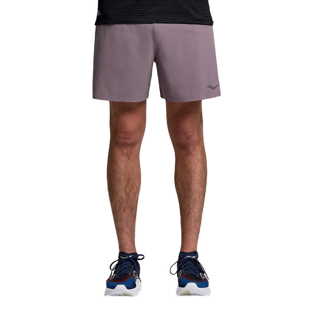 A person shown from the waist down wearing mauve athletic shorts, a black top, and blue and white running shoes against a plain white background.
