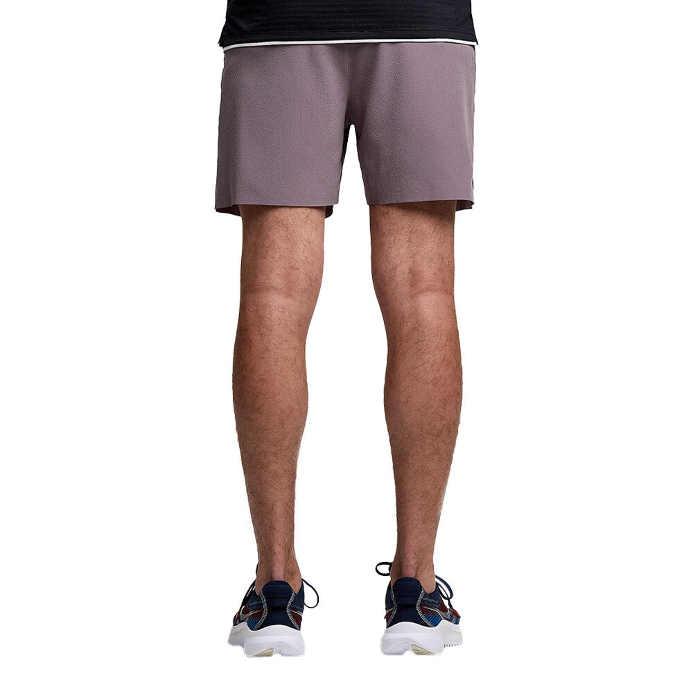 A person shown from the waist down wearing mauve athletic shorts, a dark top, and navy and white sneakers against a plain white background.