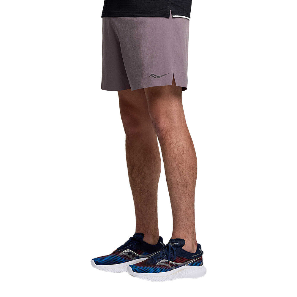 A person from waist to feet wearing mauve athletic shorts and navy running shoes against a plain white background.