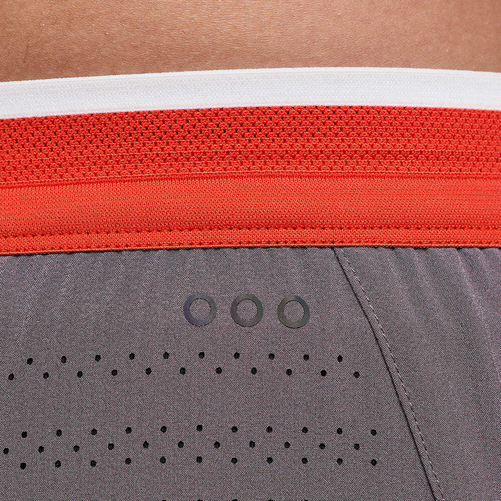 Close-up of athletic shorts showing a gray perforated fabric body, a bright orange waistband, and a white top band.