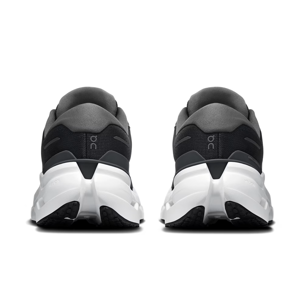Rear view of a pair of athletic sneakers in black and dark gray with chunky white midsoles, shown on a clean white background.