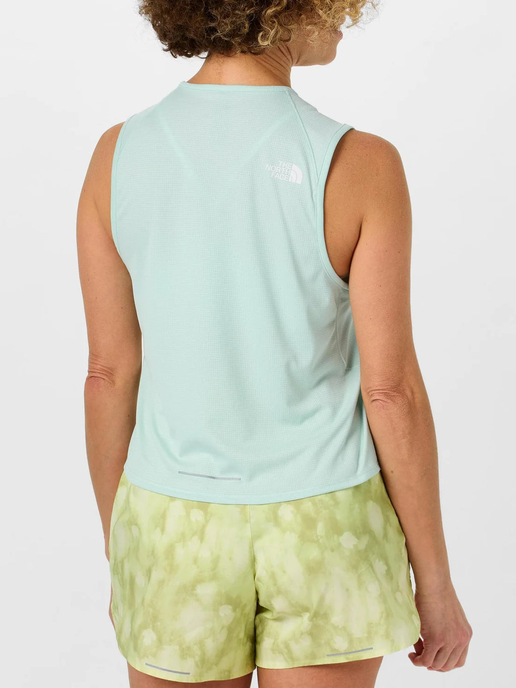 Person wearing a light blue sleeveless top and green patterned shorts on a white background