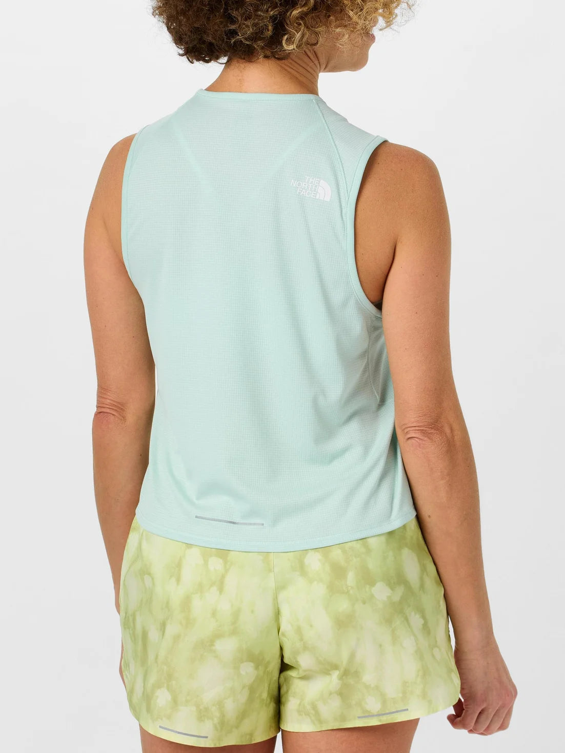 Person wearing a light blue sleeveless top and green patterned shorts on a white background