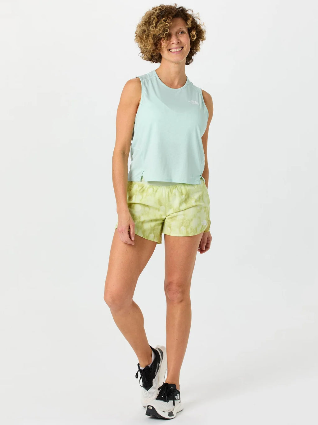 Woman wearing a light green sleeveless top and tie-dye shorts on a white background