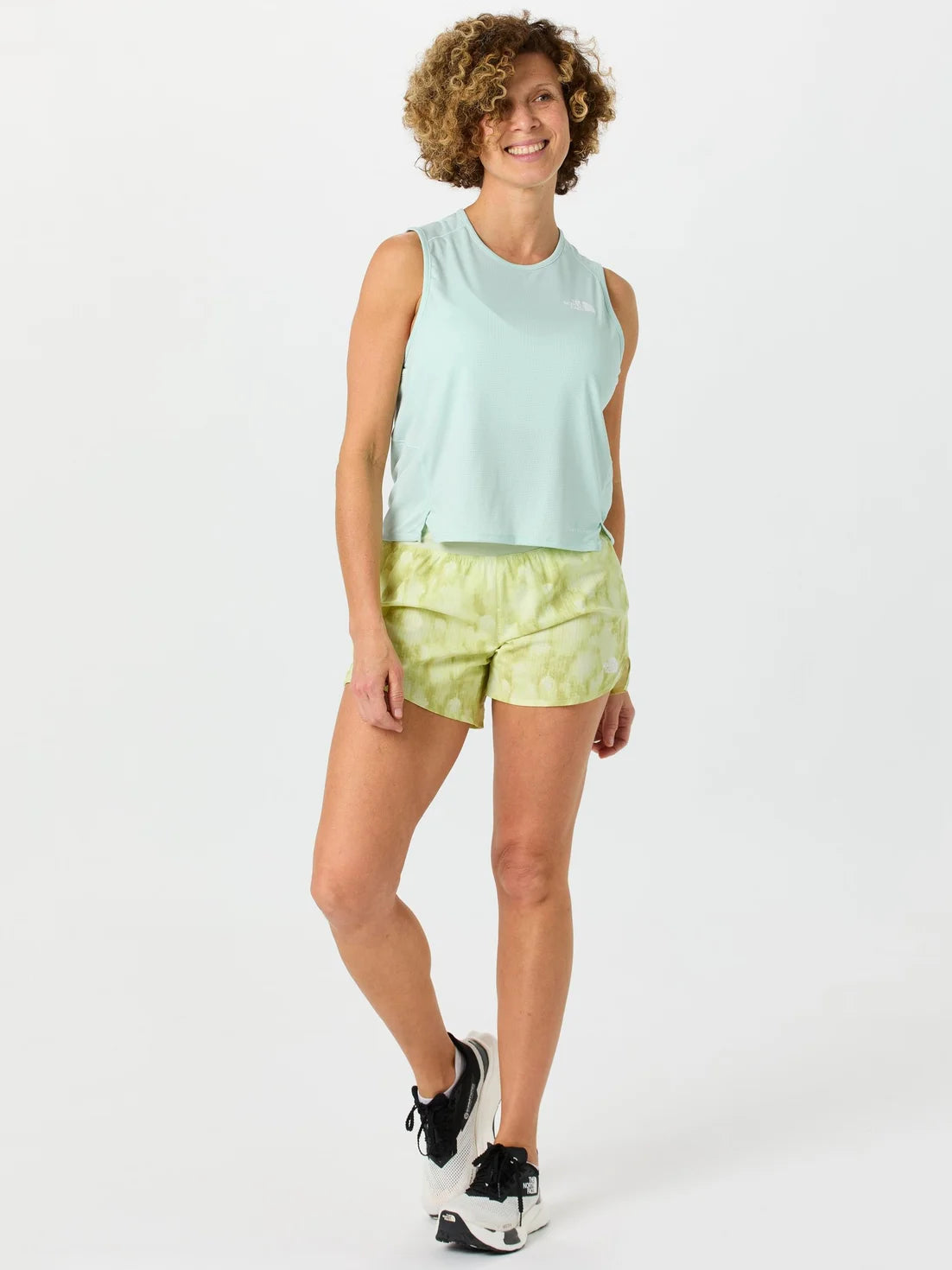 Woman wearing a light green sleeveless top and tie-dye shorts on a white background