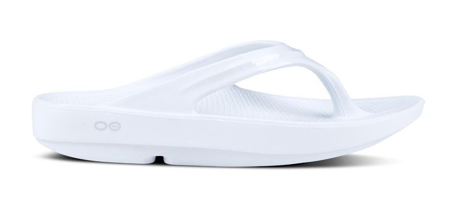 A white OOlala sandal with OOfoam technology, featuring a thong style strap and a flat, cushioned sole.