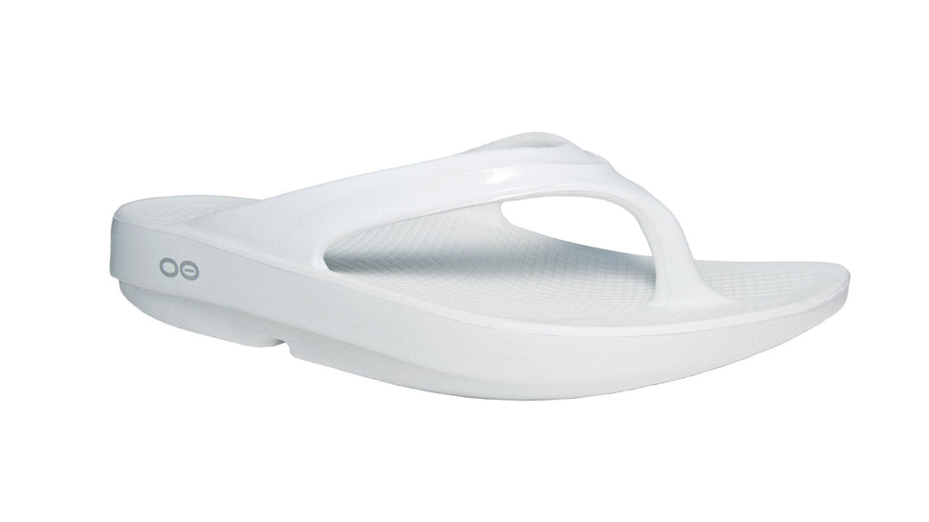 A white OOlala sandal with OOfoam technology, featuring a thong style strap and a flat, cushioned sole.